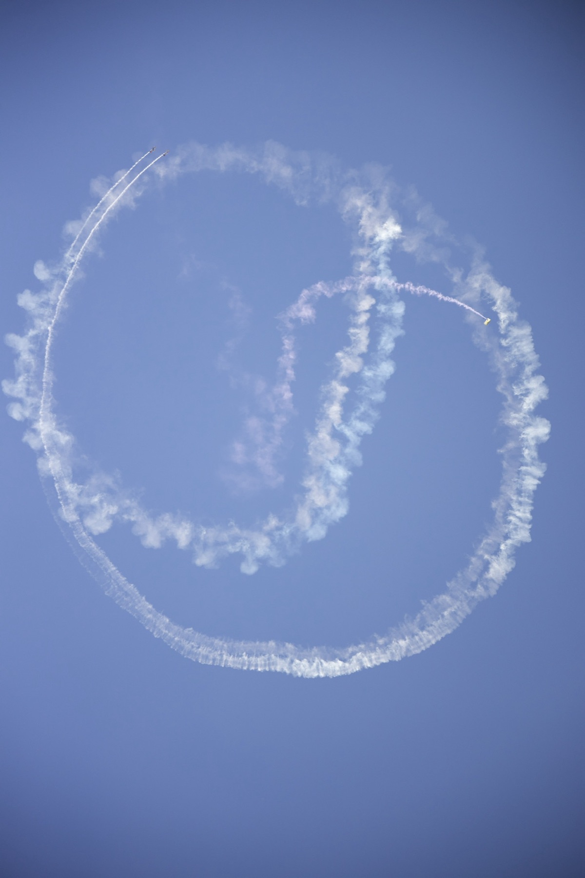 Two stunt planes draw looping smoke trails across a blue sky