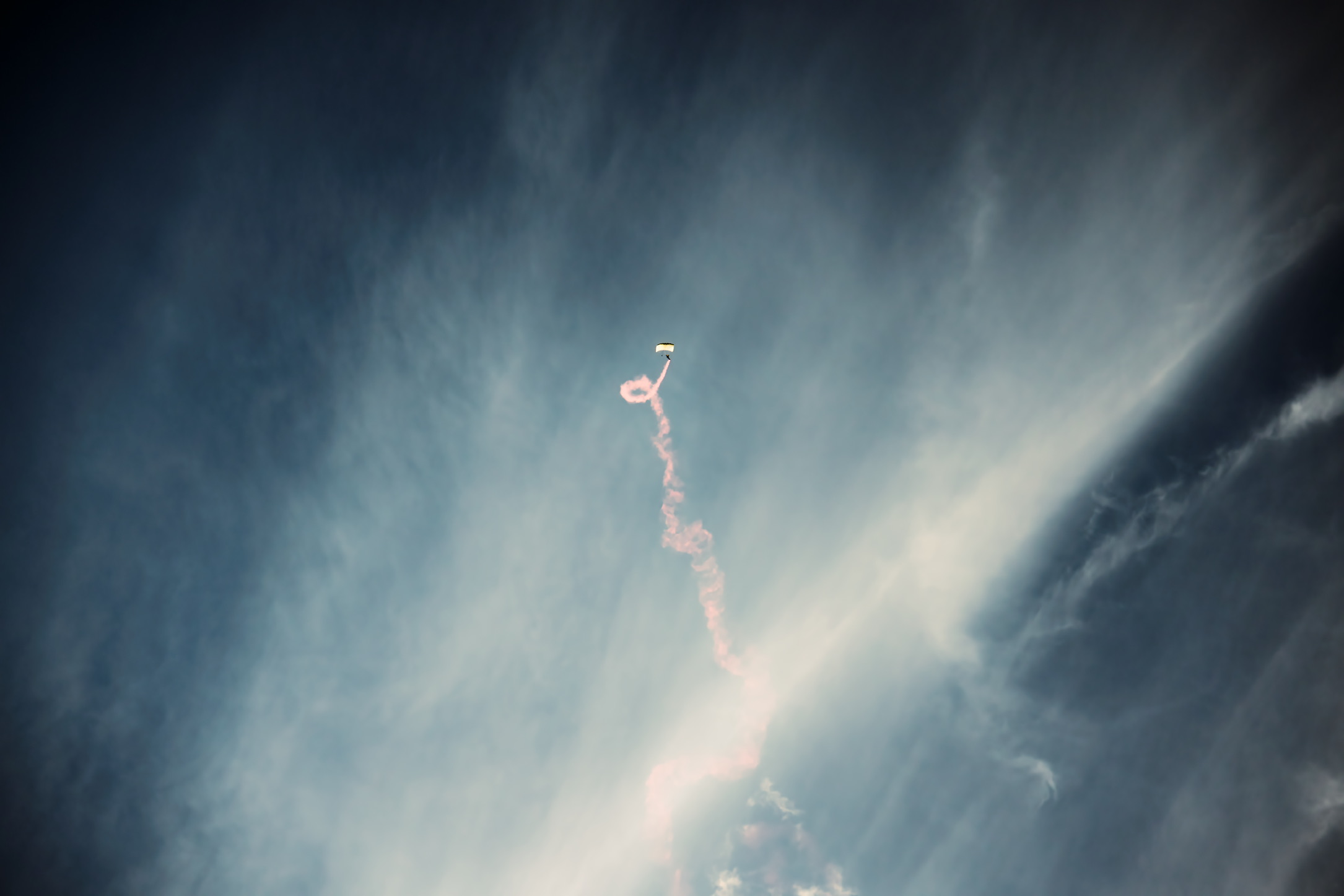 Distant parachutist trailing smoke through dramatic clouds