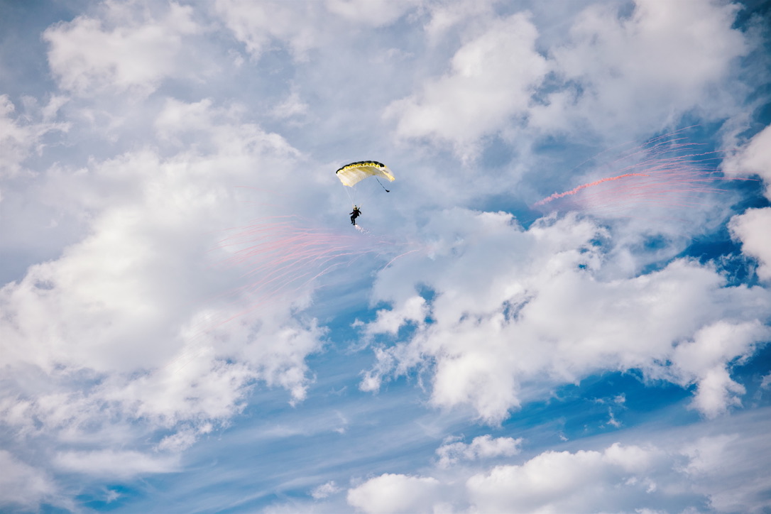 Parachutist in clouds with pink smoke trails